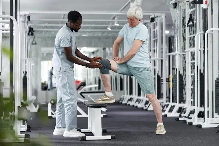 physiotherapist working with elderly man with knee injury at clinic 