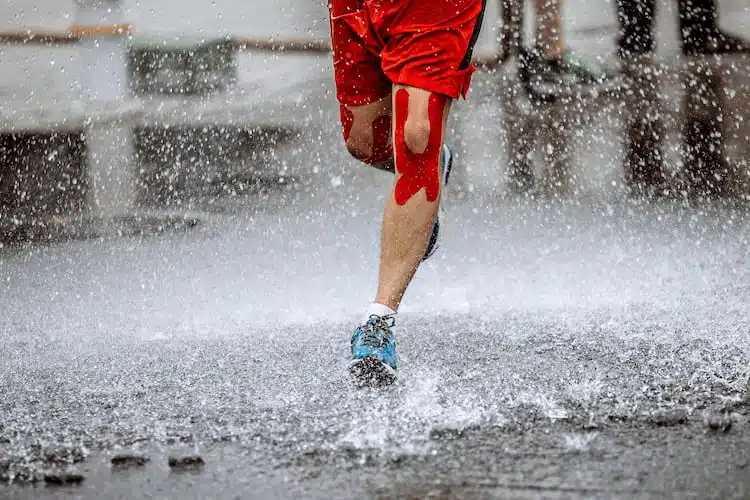 athlete running in the rain with knee sports  kinesio tape