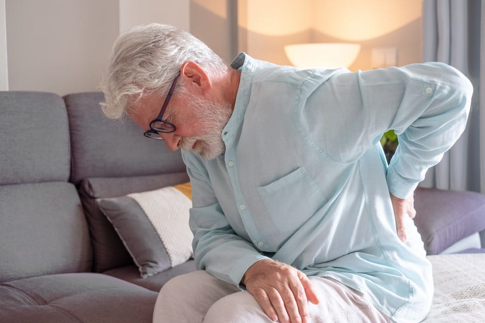 old elderly man sitting on the couch holding his back from pain of degenerative disc disease