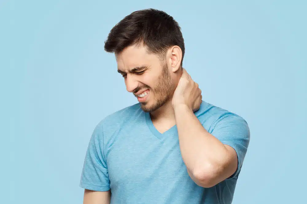 man in blue shirt touching his neck from pain of whiplash