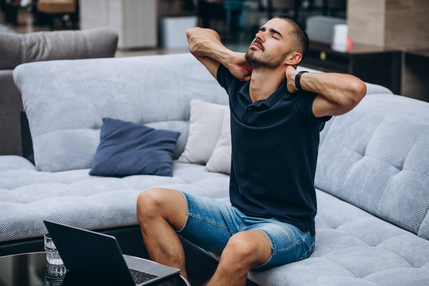 Close-up of a man clutching his neck in pain while sitting on a sofa with a laptop, illustrating the effects of poor posture and tech neck.