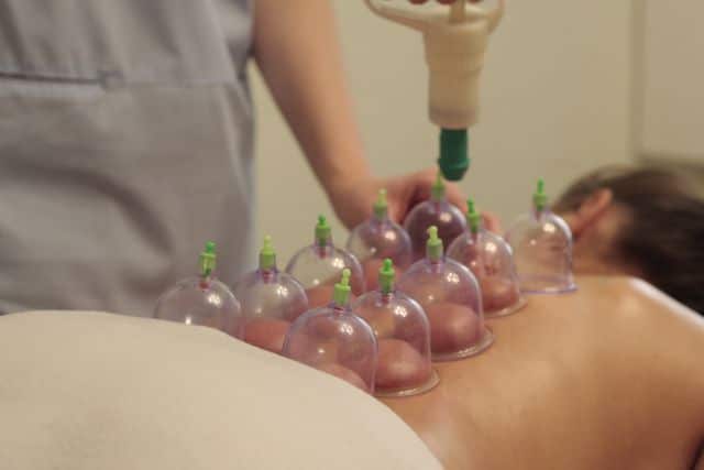 A practitioner applying a suction pump to plastic therapeutic cups placed along the back of a patient lying face down.