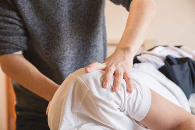 A chiropractor placing a firm hand on the upper back and shoulder of a patient lying face down to deliver a spinal adjustment.