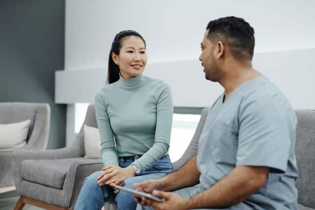 A sports injury clinician in scrubs reviewing a tablet treatment plan with a patient in a medical office lounge.