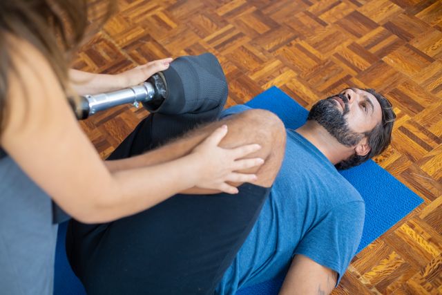 A practitioner guiding a patient's leg through a gentle hip rotation exercise on a yoga mat.