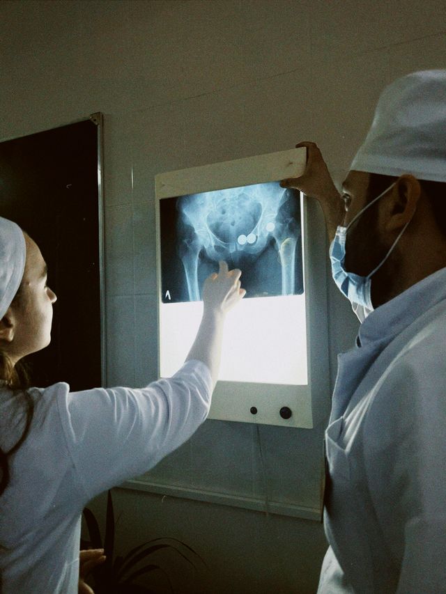 Two medical professionals in scrubs examining a pelvic and hip joint X-ray on a light box.