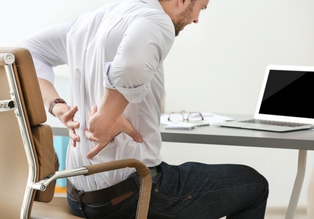 Office worker experiencing lower back pain and posture strain at a desk.